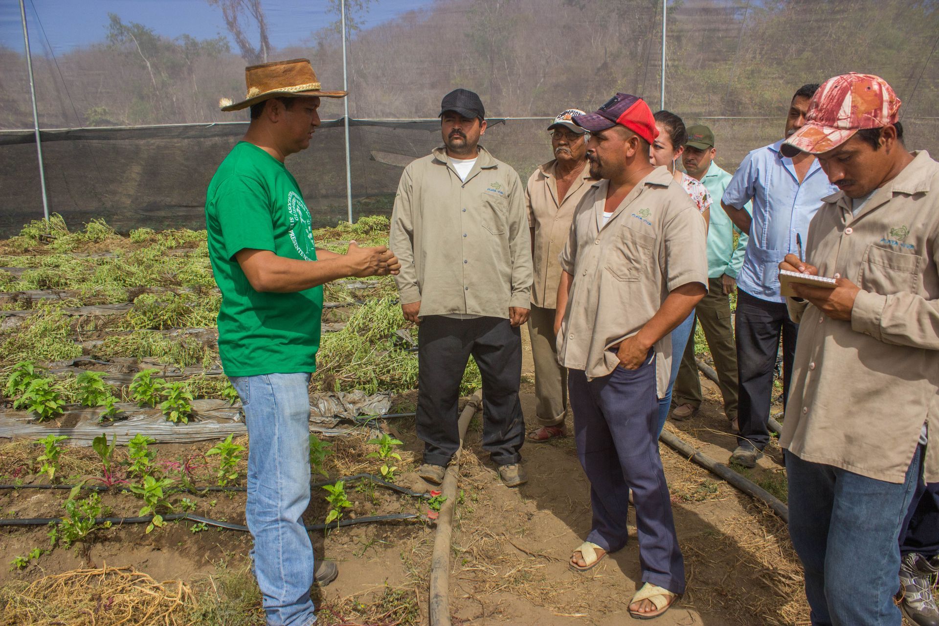 A man in a green shirt is talking to a group of men in a field.