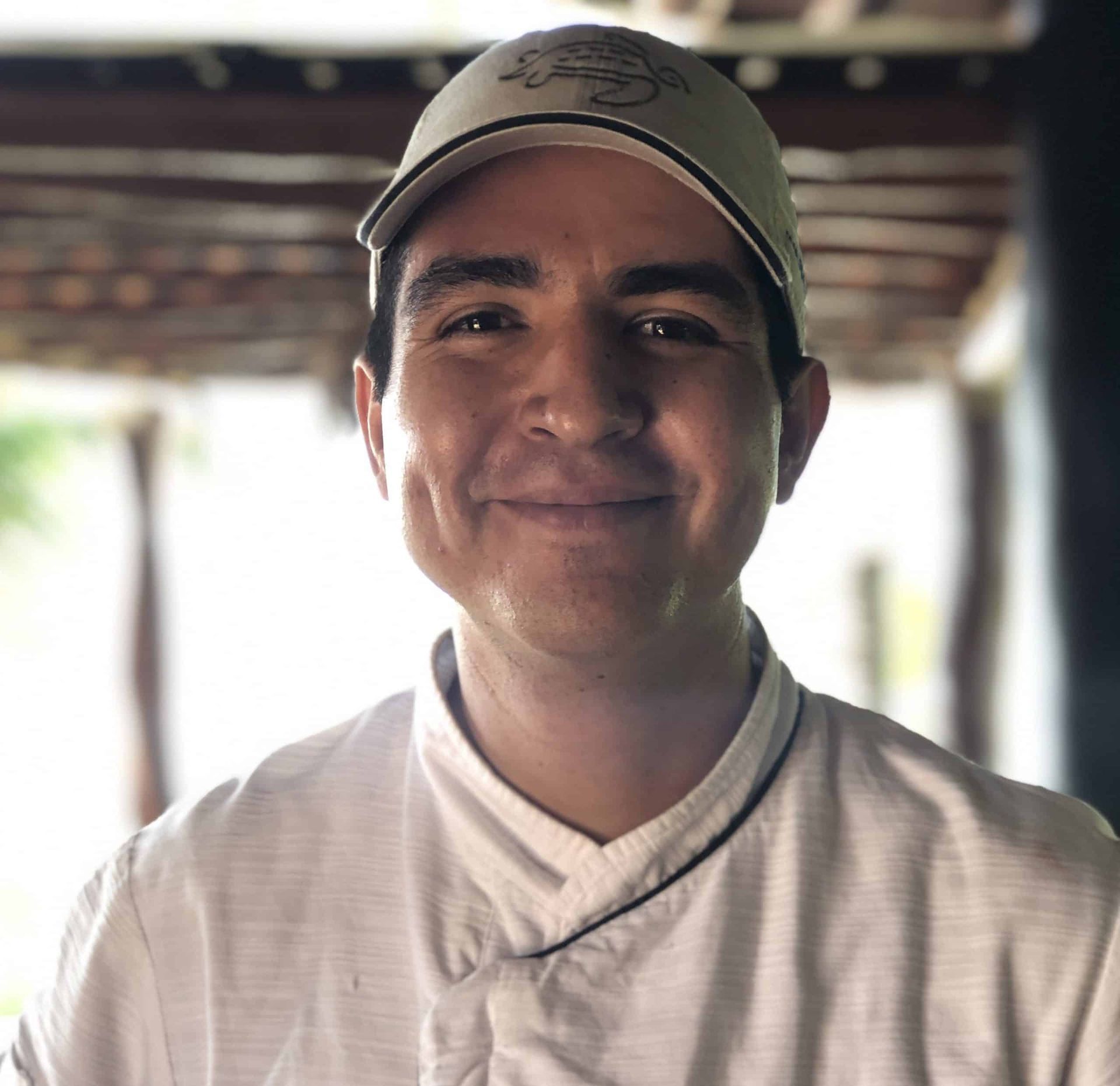 A man wearing a hat and a chef 's uniform is smiling for the camera.