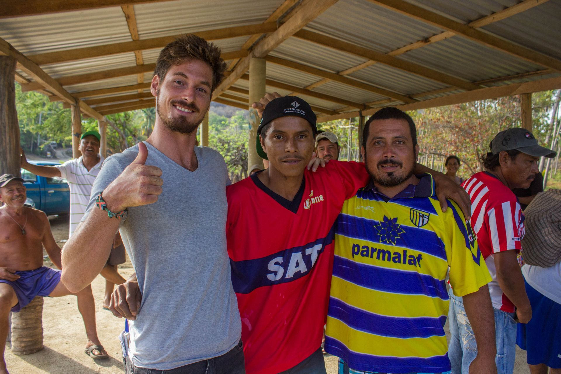 Three men are posing for a picture and one of them is wearing a red shirt that says sat.