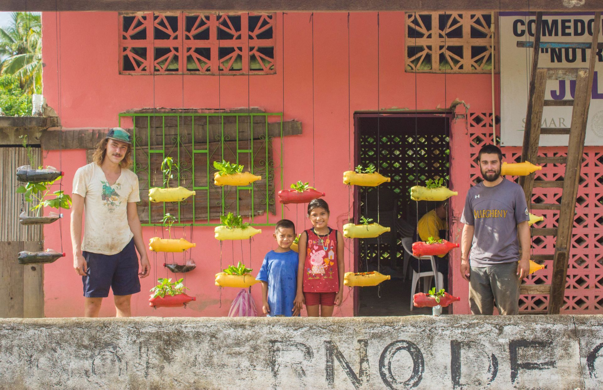 A group of people standing in front of a pink building with a sign that says comedo