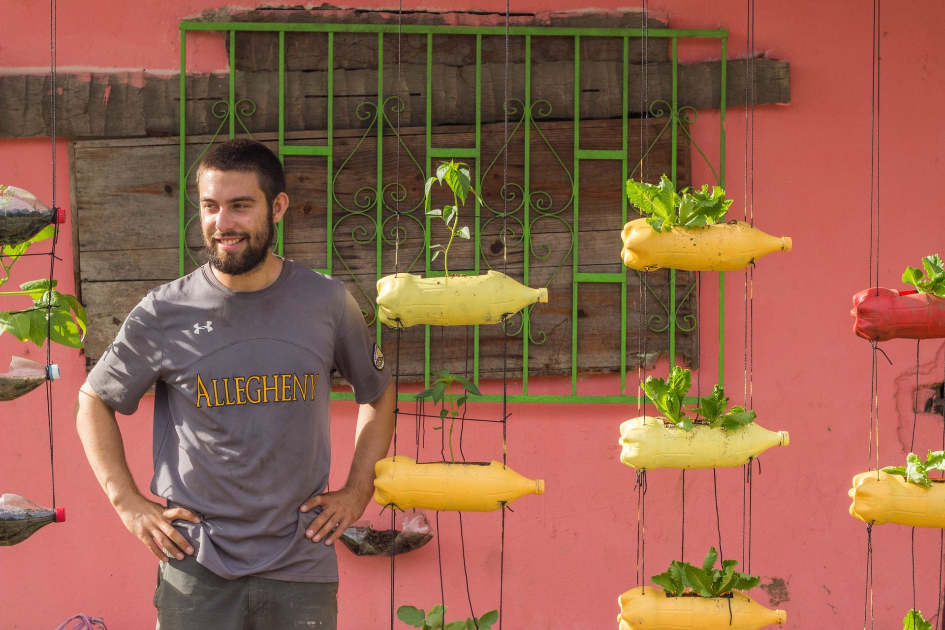 A man is standing in front of a wall with plants hanging from it.