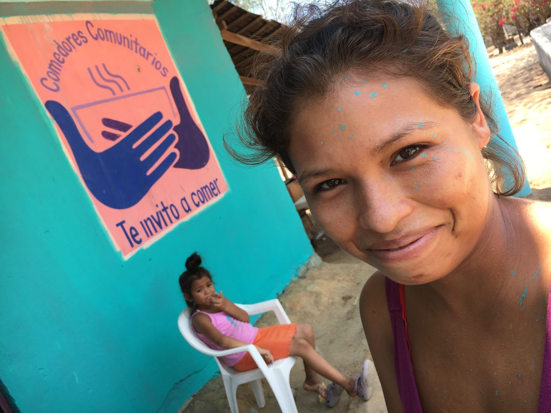 A woman is smiling in front of a sign that says te invito a comer