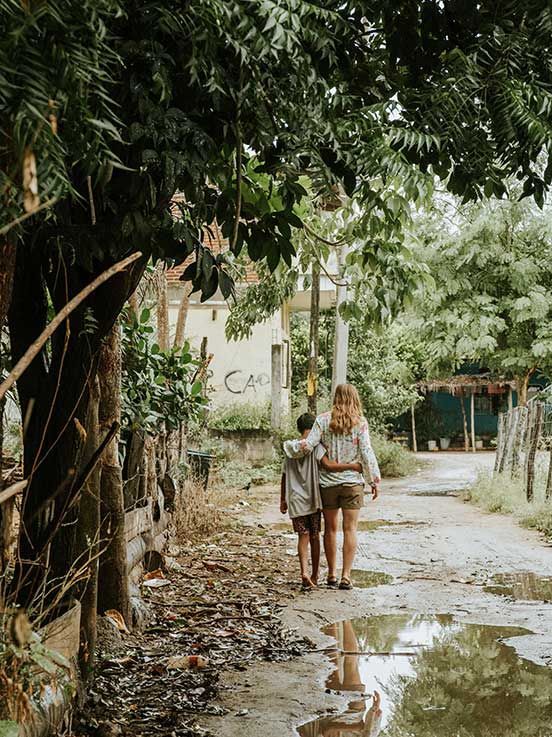A woman and a child are walking down a dirt road.