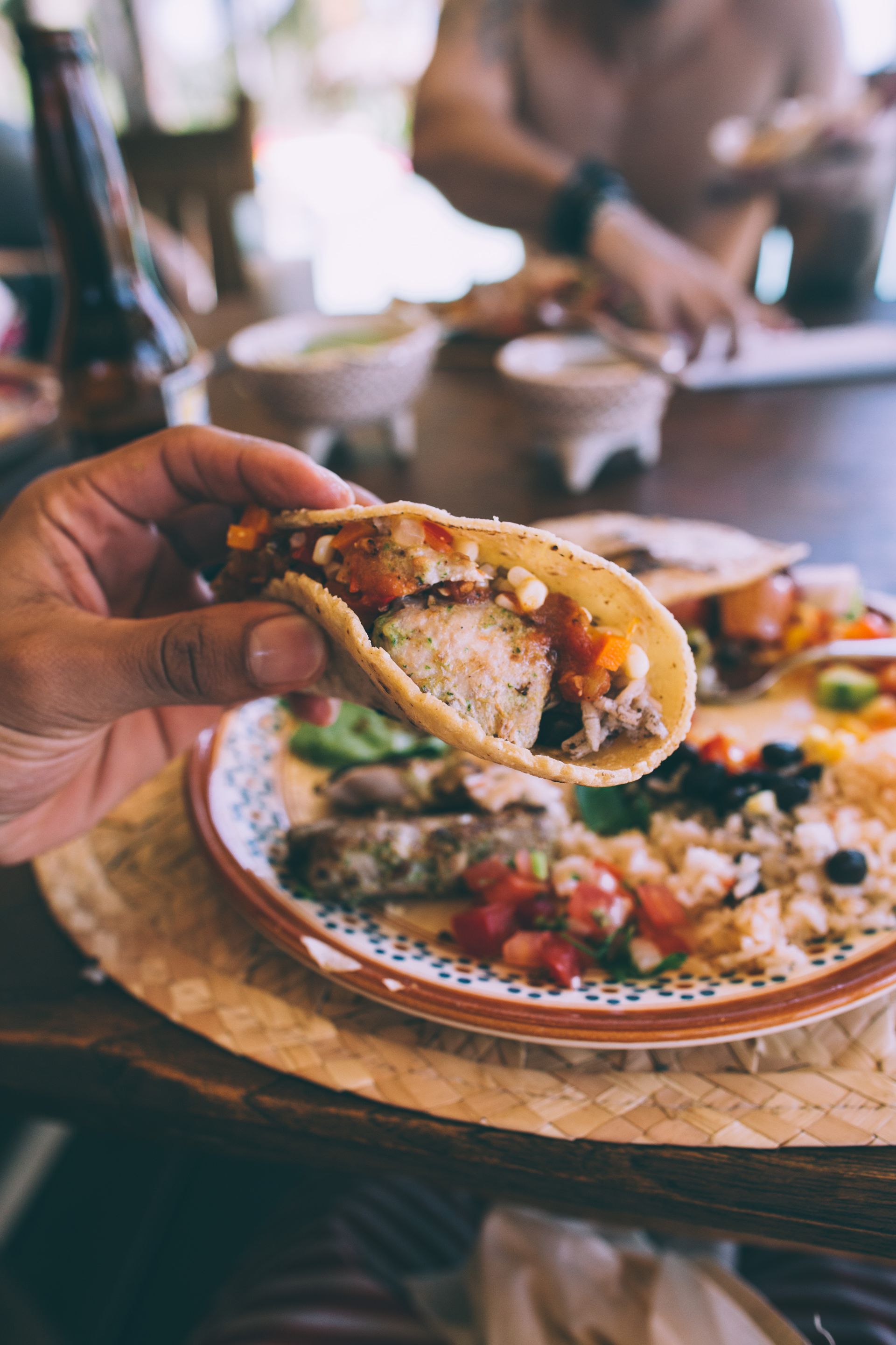 A person is holding a taco in front of a plate of food.