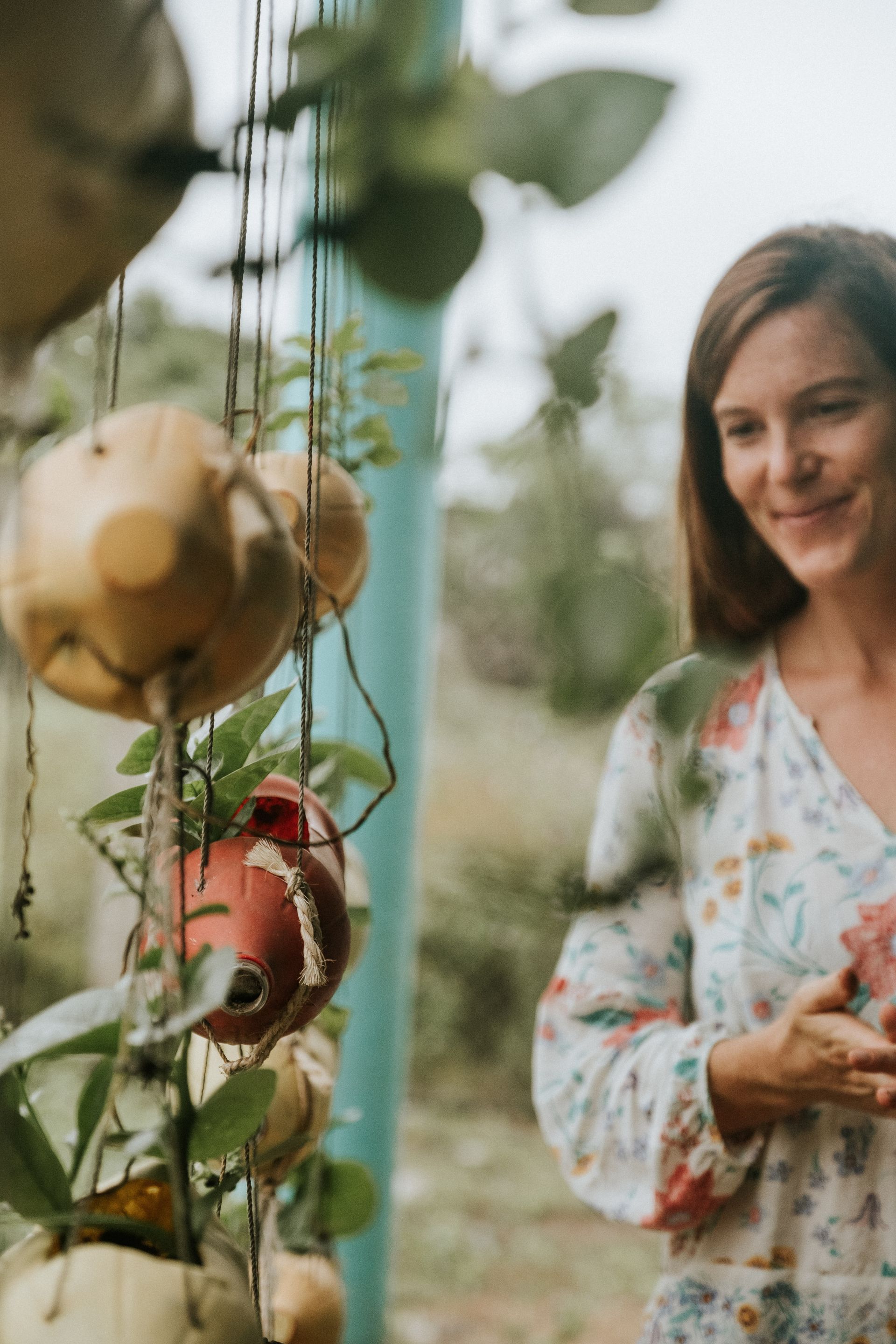 A woman is standing in front of a bunch of pumpkins hanging from a tree.