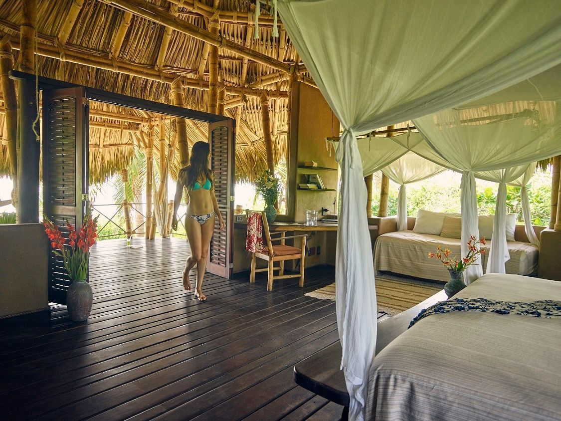 A woman in a bikini is walking into a room with a canopy bed.