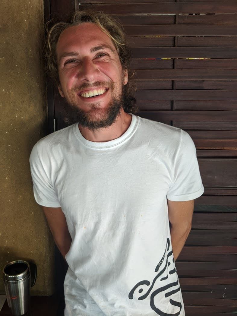 A man with a beard is wearing a white shirt and smiling