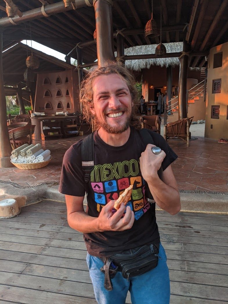 A man in a black shirt is holding a hot dog and smiling.