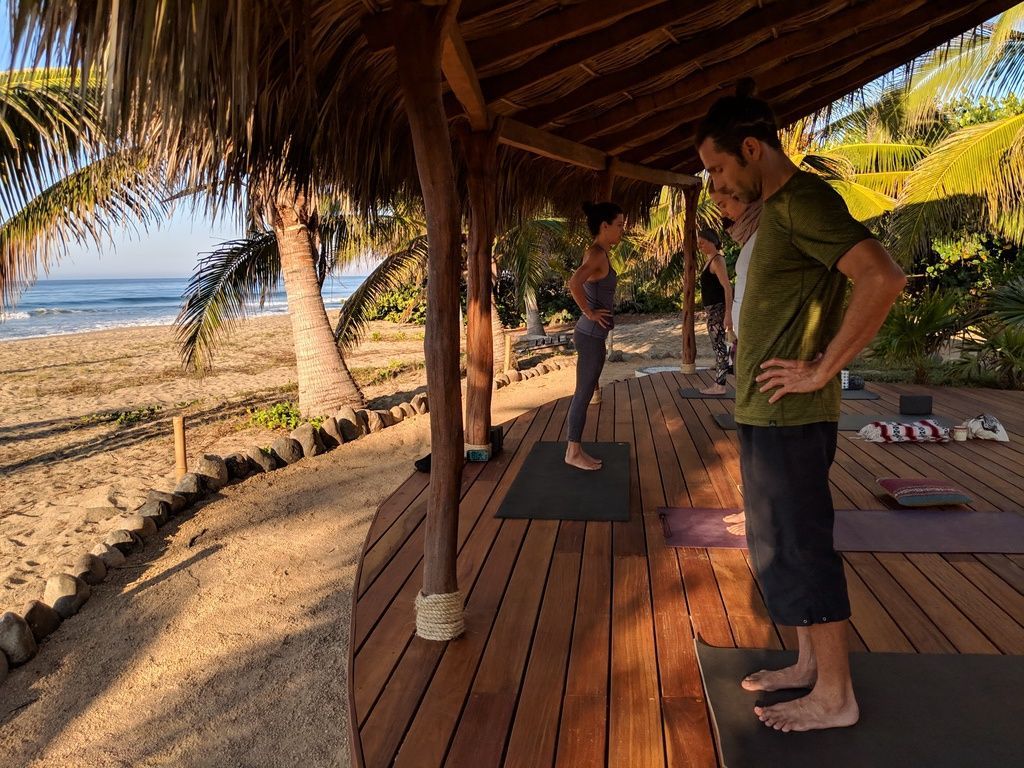 A man and a woman are standing on yoga mats on a wooden deck.