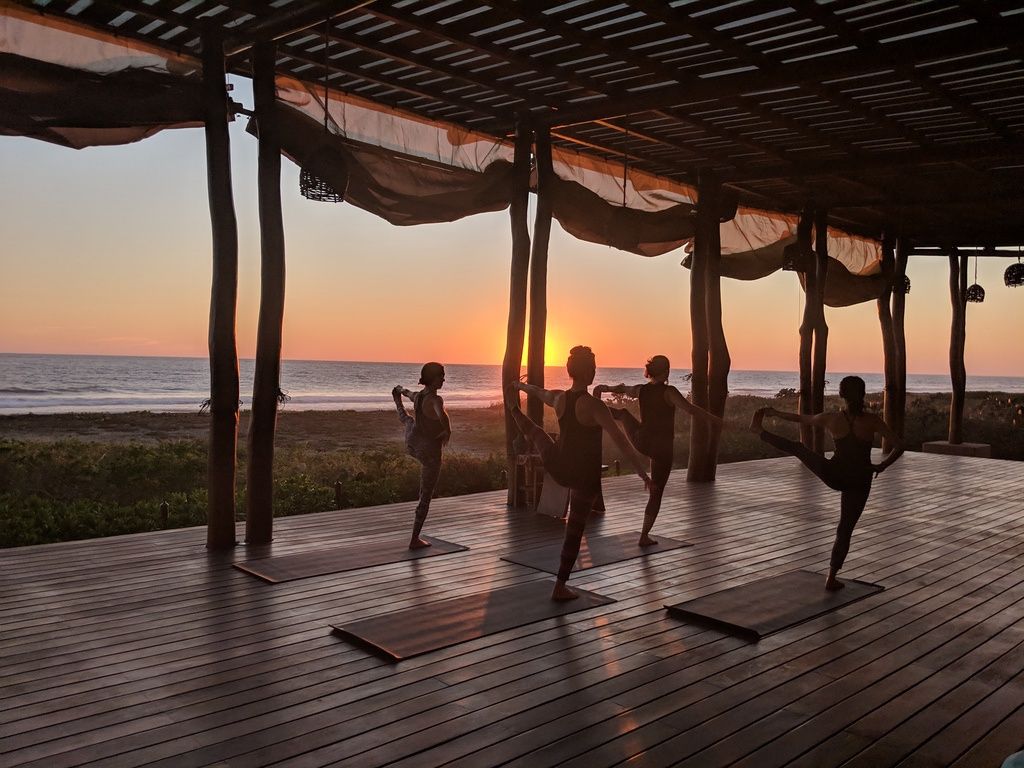 A group of people are doing yoga on a deck at sunset.