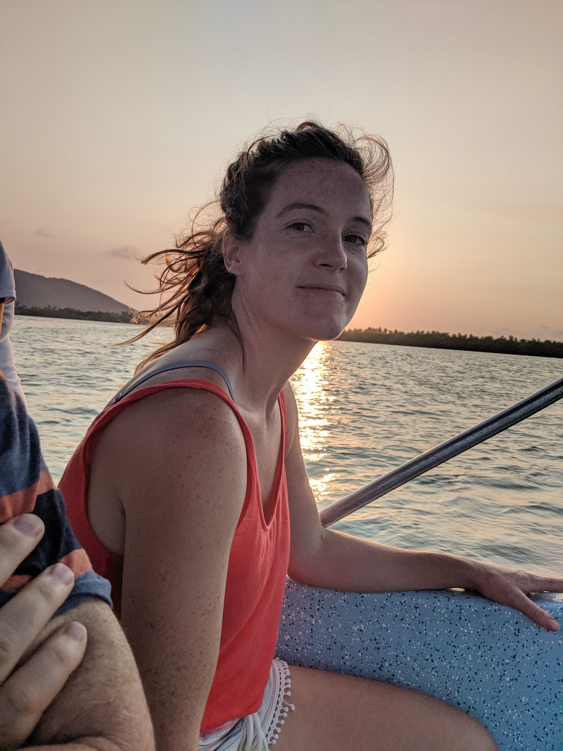 A woman is sitting on a boat in the water at sunset.