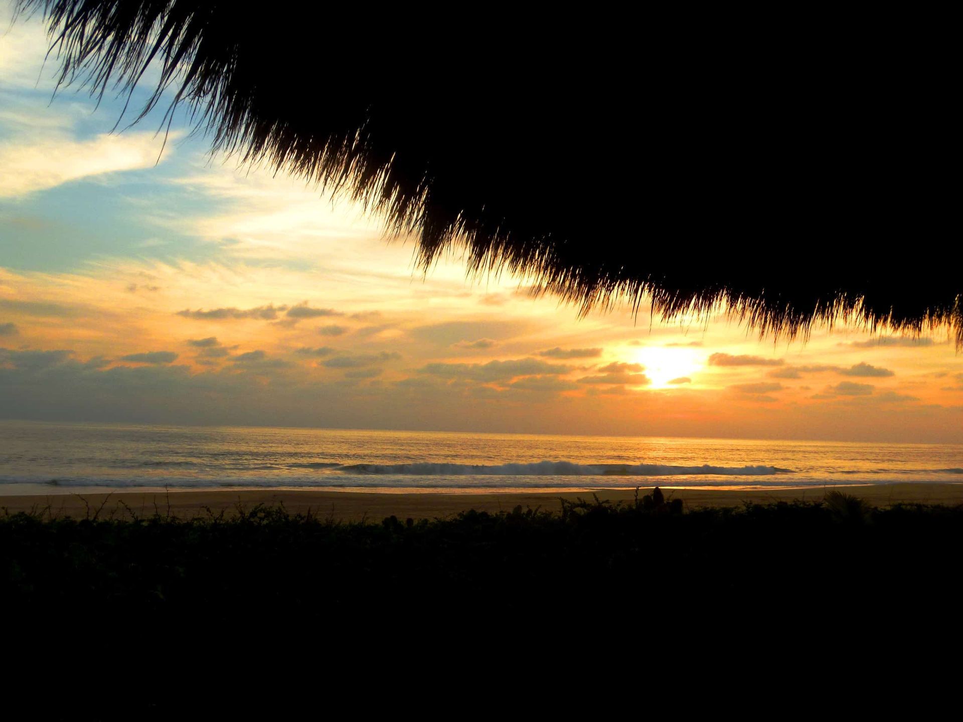 A sunset over the ocean with a thatched roof in the foreground