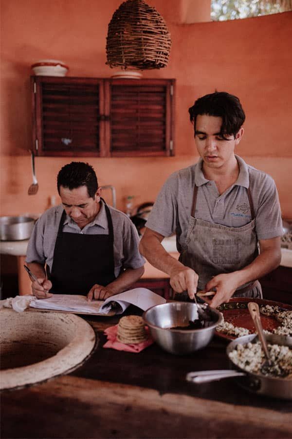 Two men in aprons are preparing food in a kitchen.