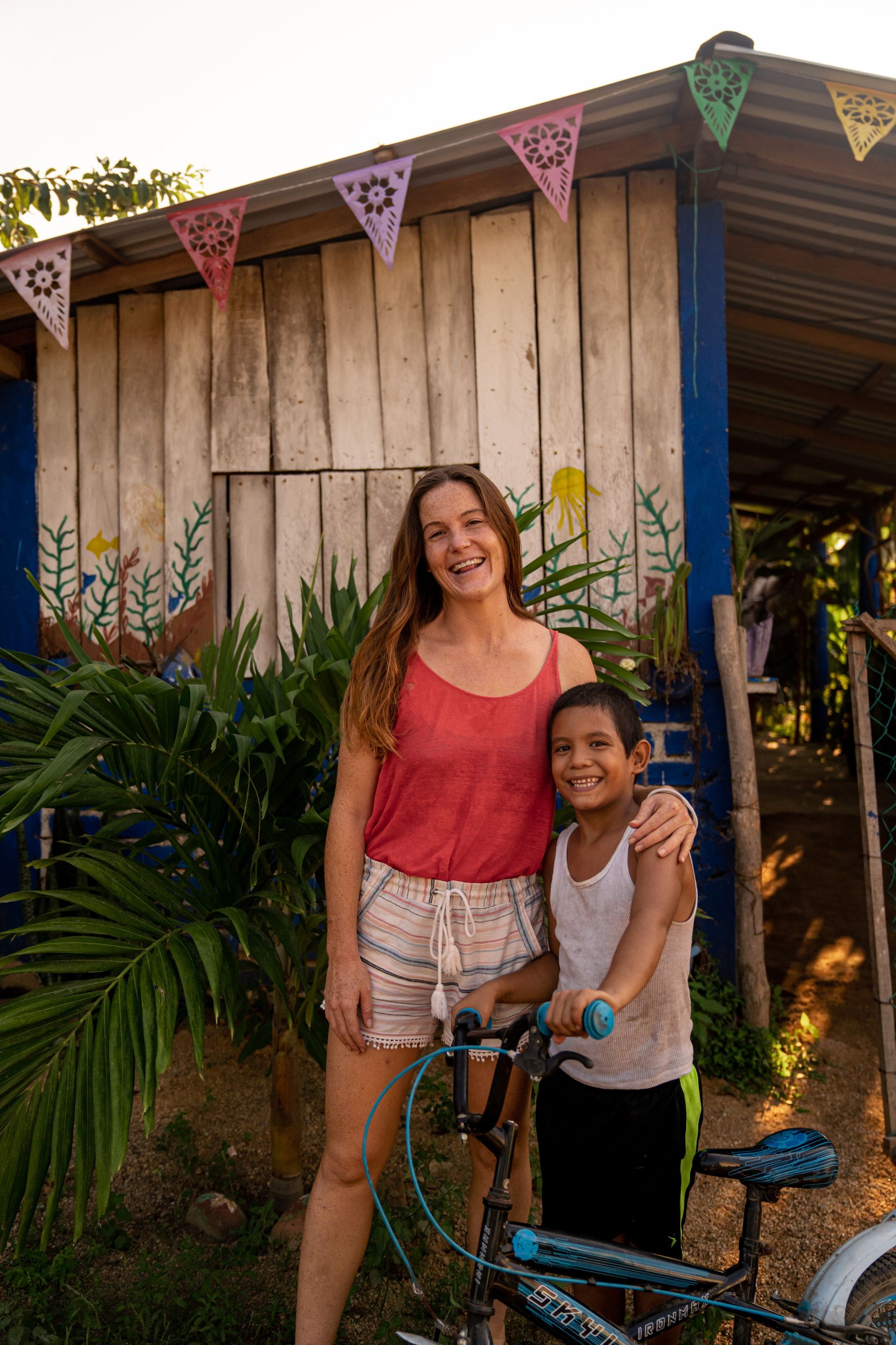 A woman and a boy are standing next to a bicycle in front of a house.