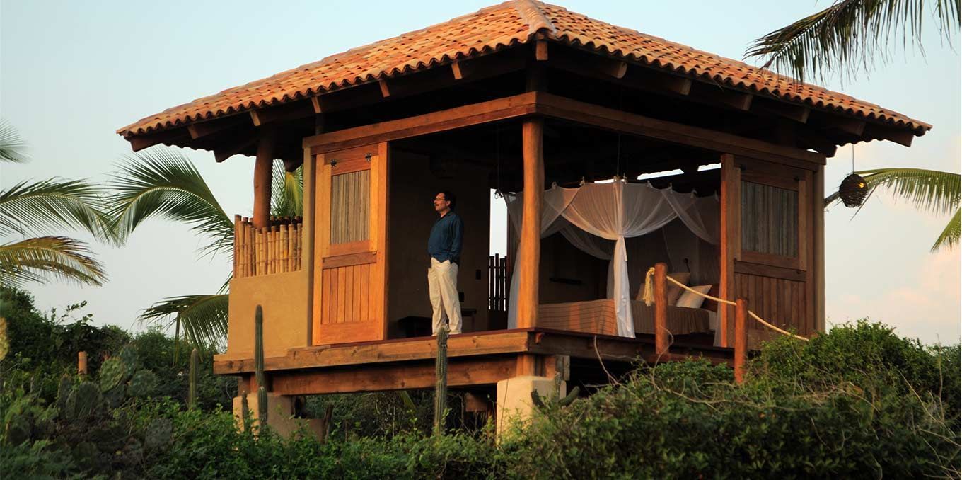 A man is standing on the porch of a small wooden house.
