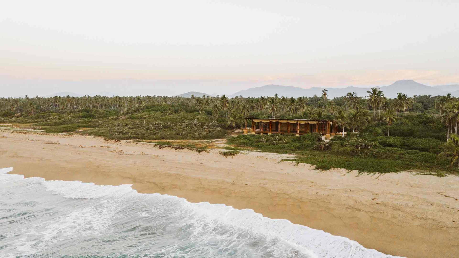 An aerial view of a beach with a house in the distance.