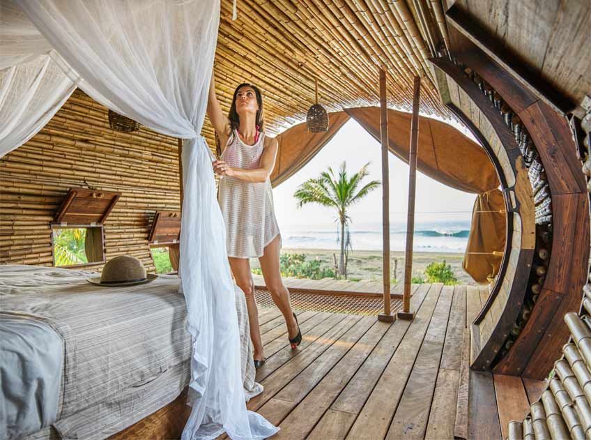 A woman in a white dress is standing next to a bed in a bamboo hut.