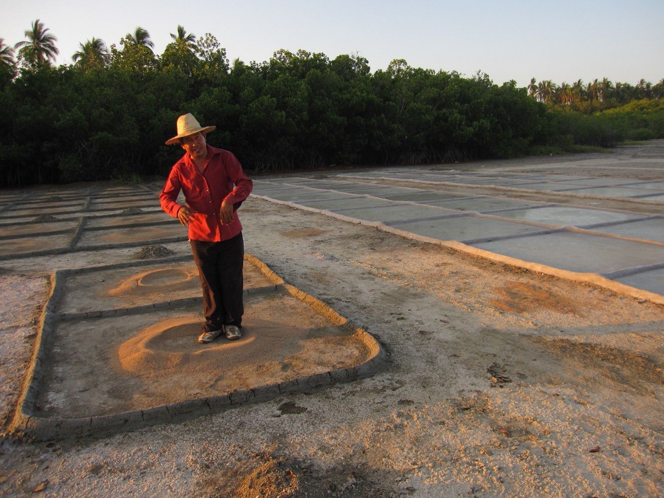 A man in a straw hat is standing on a dirt road