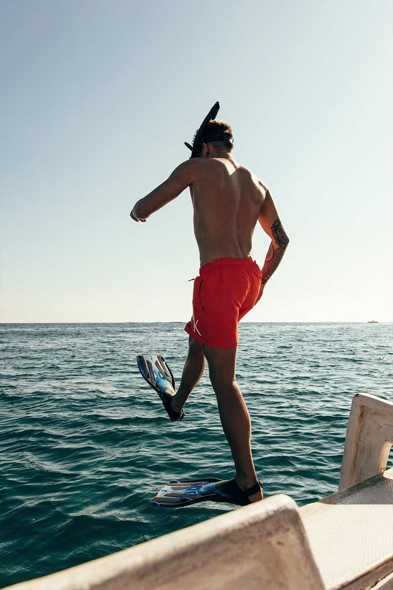 A man in red shorts is jumping into the ocean from a boat.