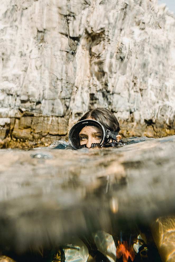 A woman is swimming in the ocean with a cliff in the background.