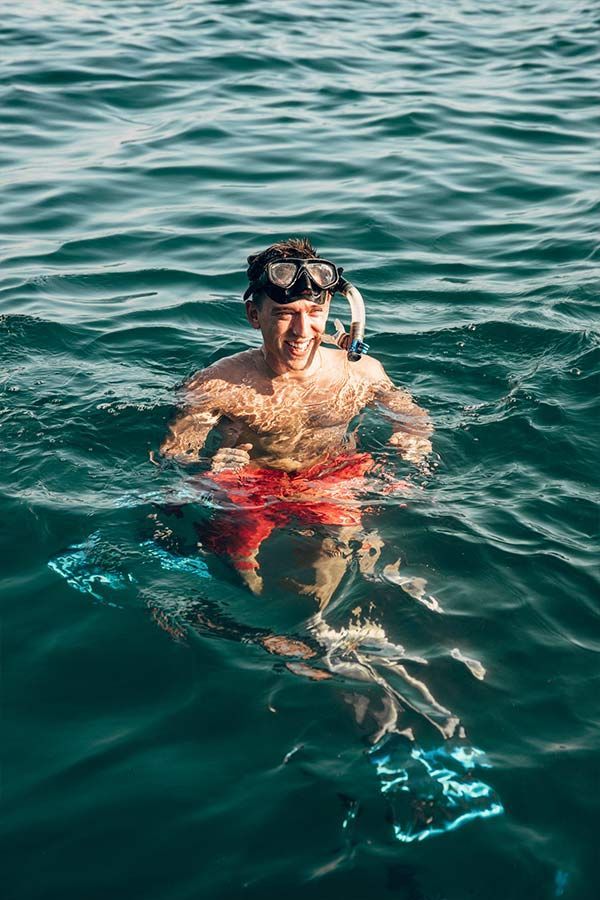 A man is swimming in the ocean with a mask on his face.