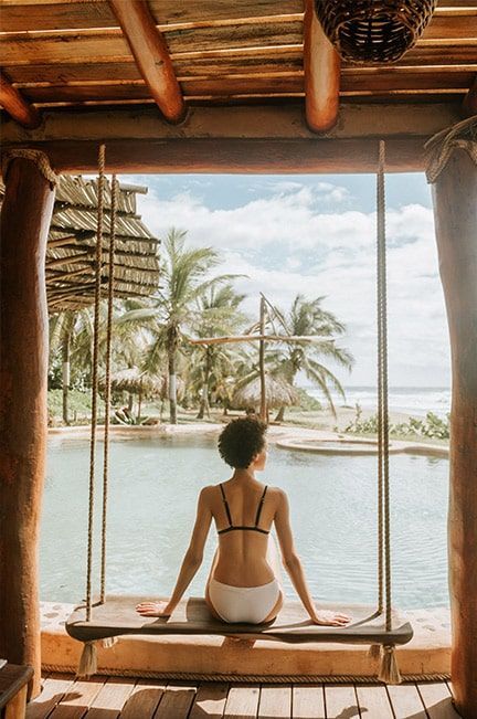 A woman in a bikini is sitting on a swing overlooking a pool.