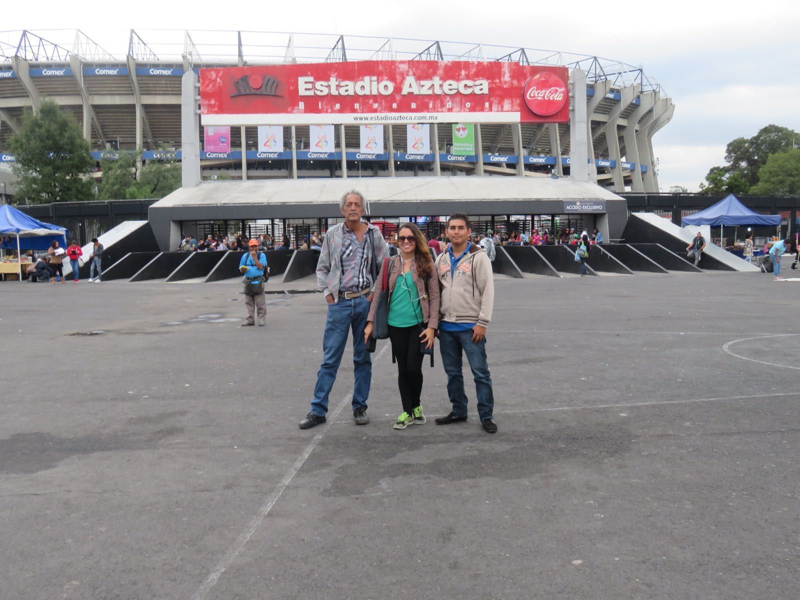 Three people standing in front of a stadium that says estadio azteca