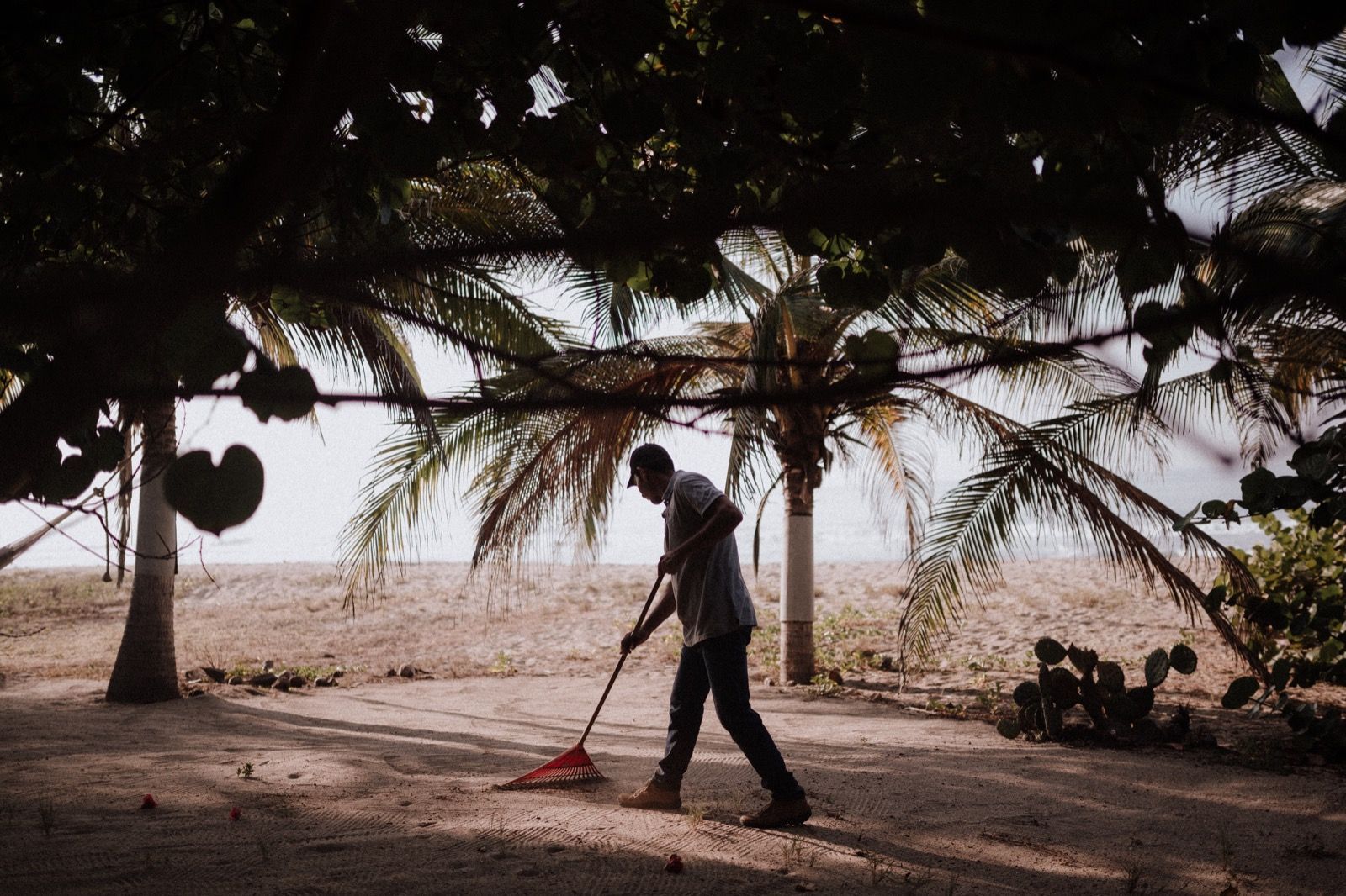A man is sweeping the sand on the beach with a broom.