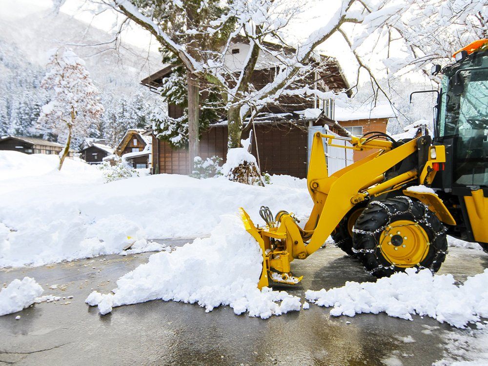 A yellow snow plow is clearing snow from a driveway.