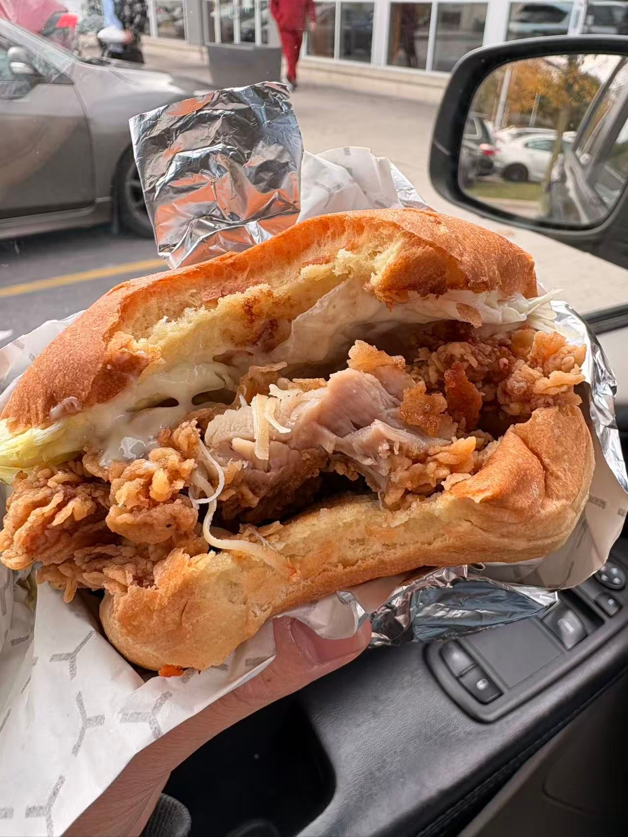 Partially eaten fried chicken sandwich in a car, wrapped in foil on the passenger seat.