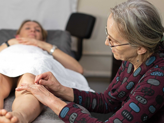 An acupuncturist needling a point in the leg of a woman lying on a couch