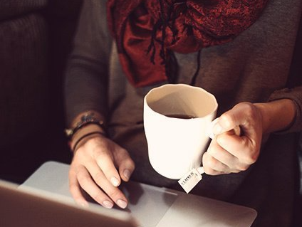Woman using her laptop and holding a cup of tea