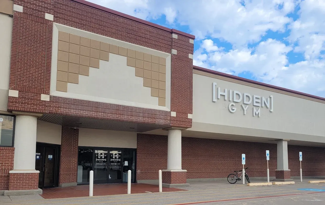 Front of Hidden Gym storefront with brick facade, tan sign, and covered entrance under a blue sky
