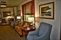 Cozy lounge area with seating, artwork, and natural light from a window with wooden blinds.