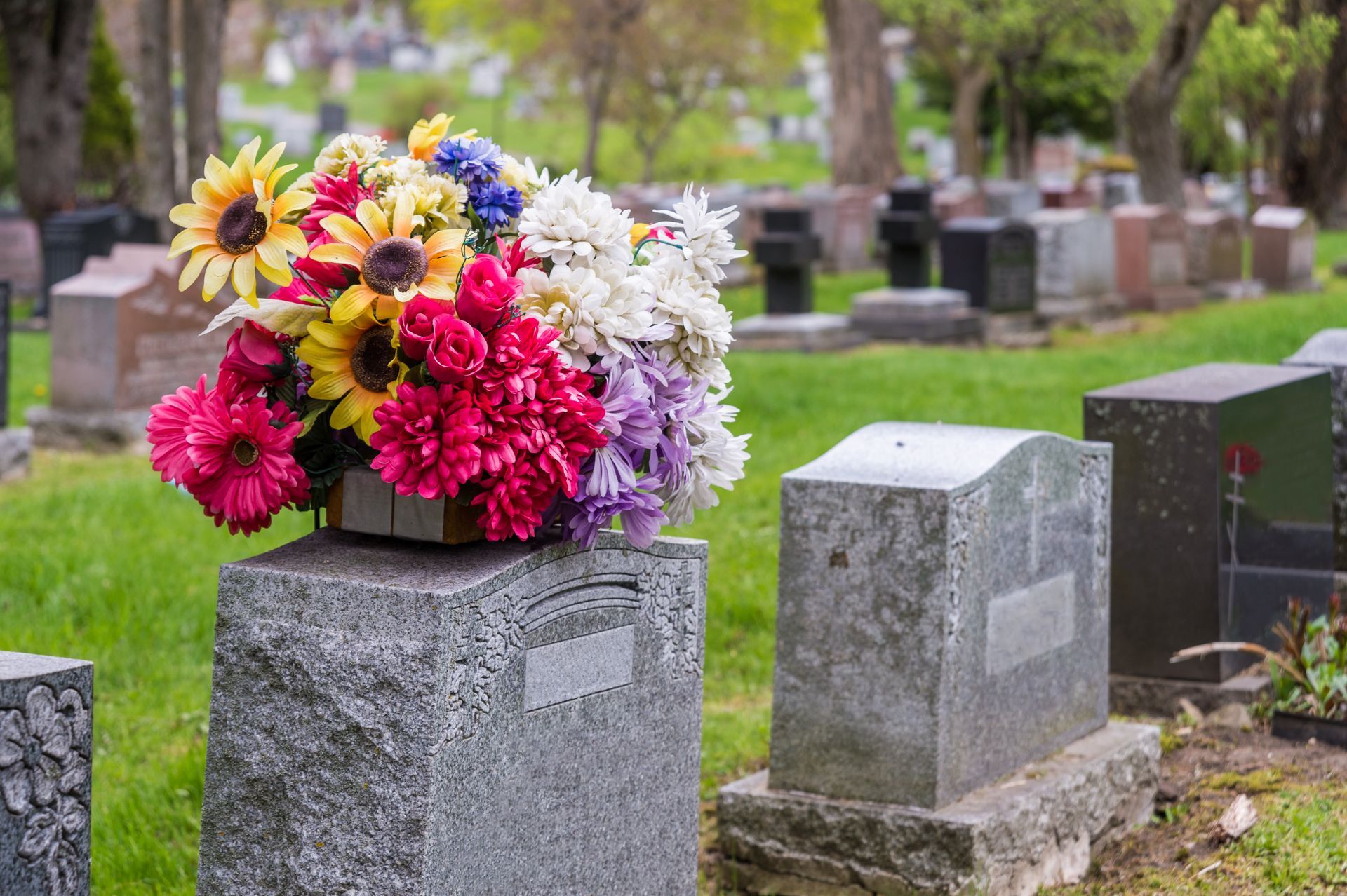 Colorful flowers on a tombstone in a cemetery with other gravestones and green grass.