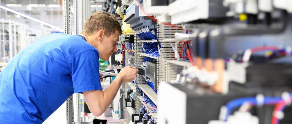A Man In A Blue Shirt Is Working On A Machine In A Factory — Wylec In Newcastle, NSW