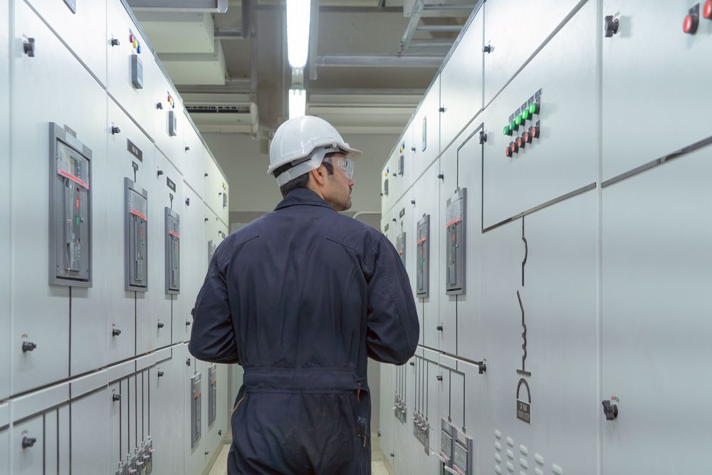 A Man In A Hard Hat Is Standing In A Hallway Looking At Electrical Panels — Wylec In Mayfield West, NSW
