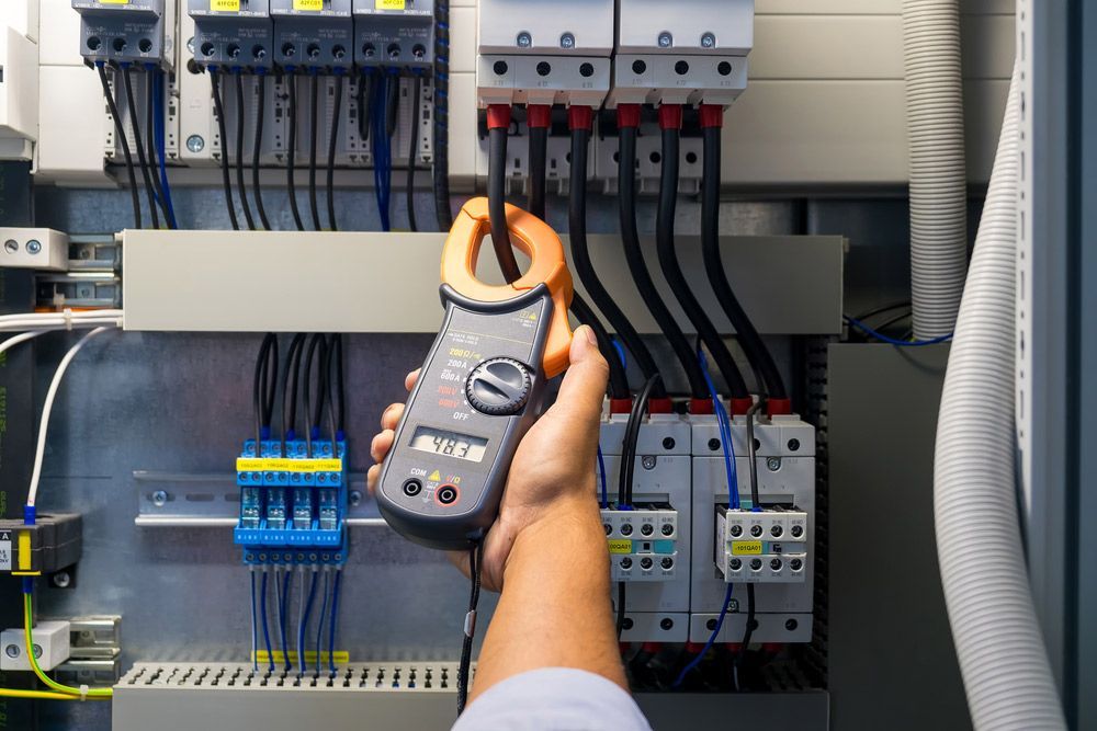 A Person Is Holding A Clamp Meter In Front Of A Electrical Panel — Wylec In Newcastle, NSW