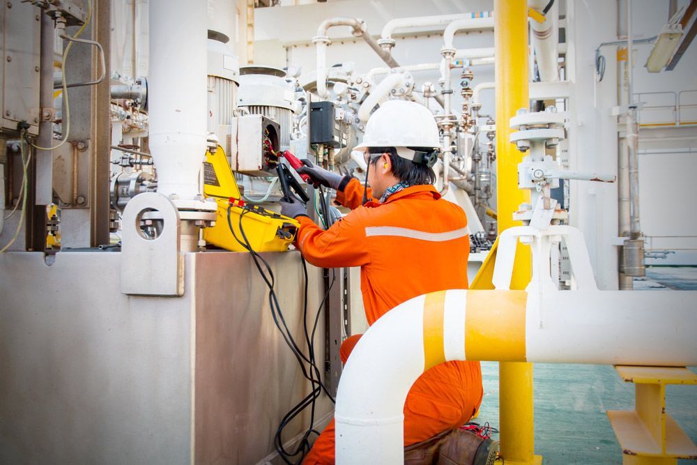 A Man Is Working On A Machine In An Oil Refinery — Wylec In Mayfield West, NSW