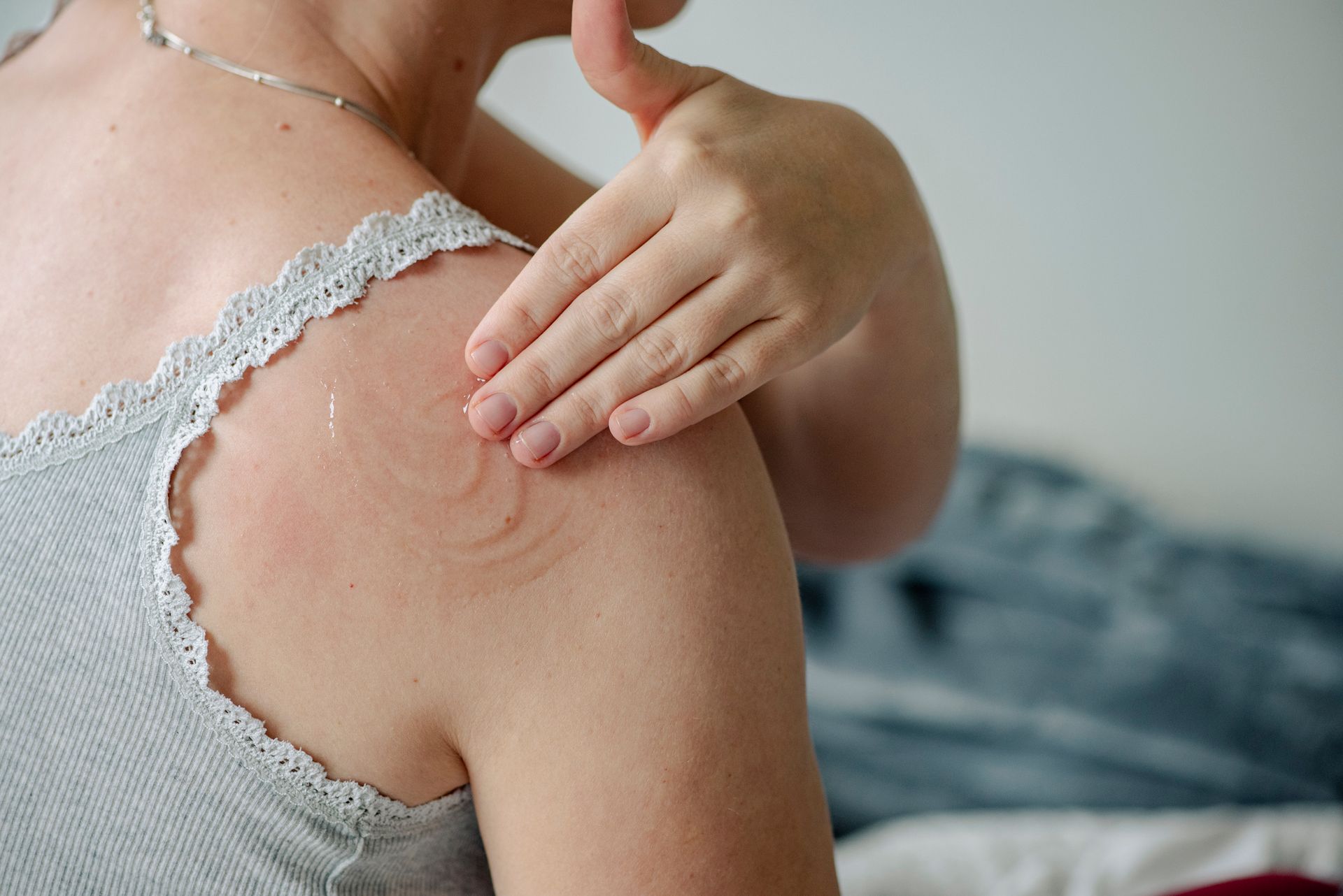 A woman is applying lotion to her shoulder.