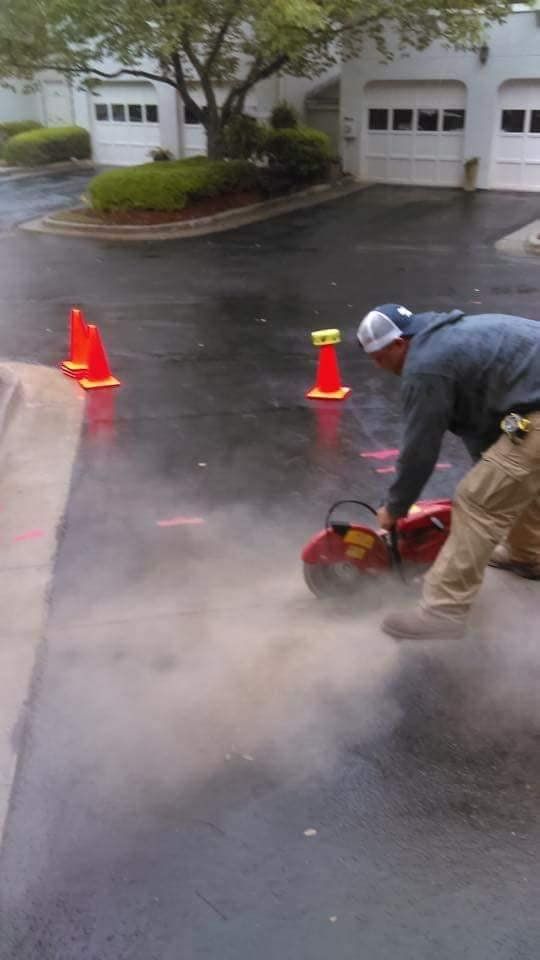 A man is cutting concrete with a circular saw in a parking lot.