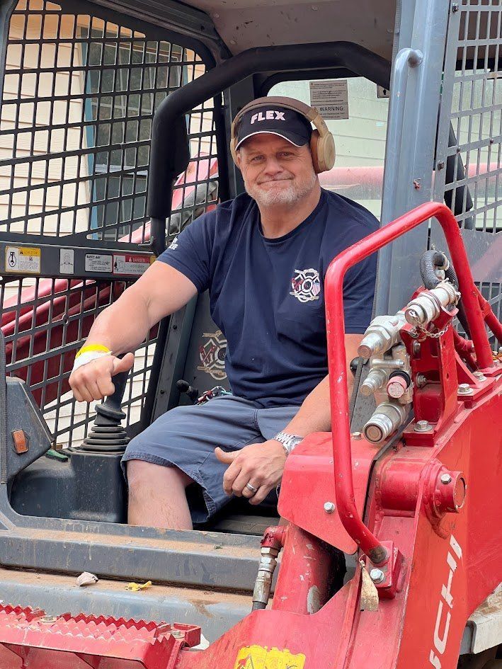 A man is sitting in a red bulldozer giving a thumbs up.
