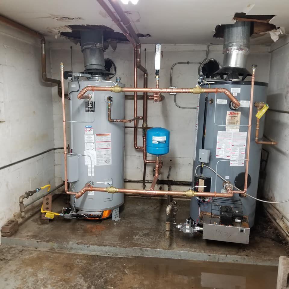 Two water heaters are in a room with copper pipes