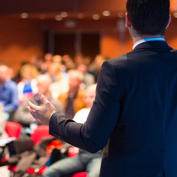 A man in a suit is giving a presentation to a crowd of people