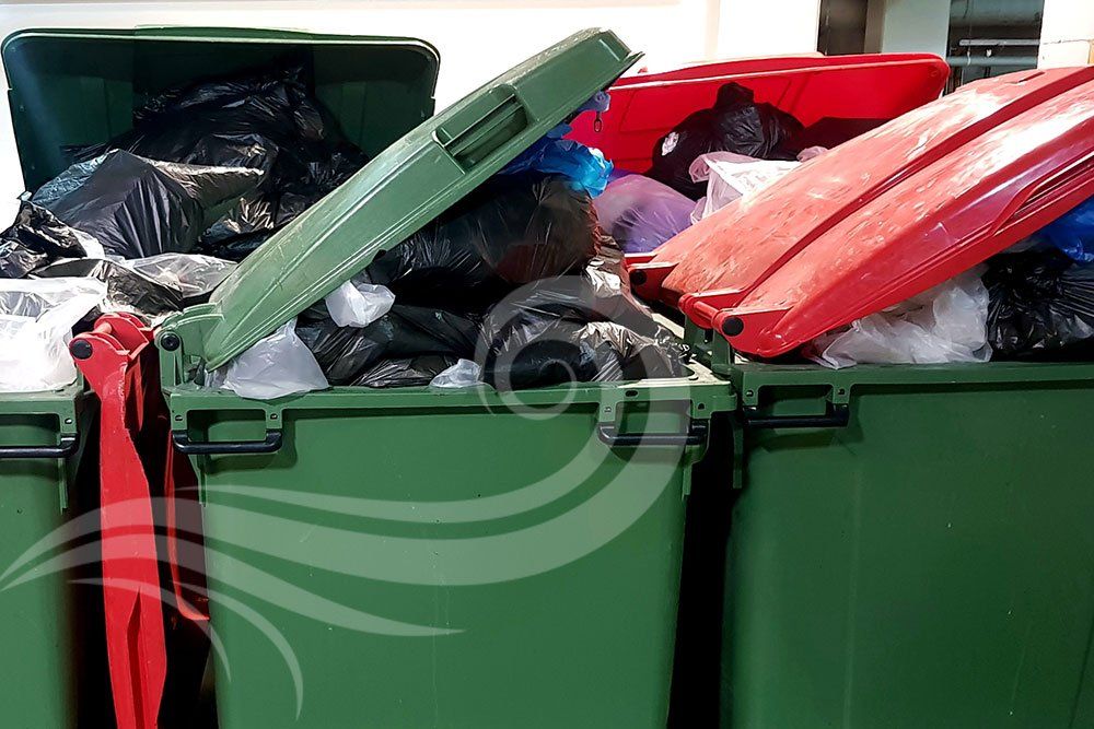 A green trash can with a red lid is filled with trash.