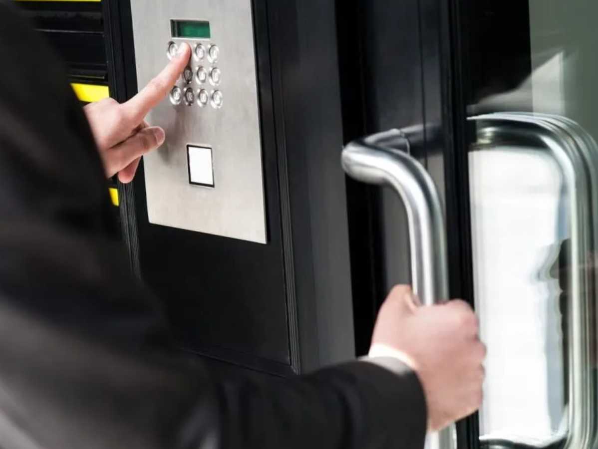 Person in a suit entering building, punching keypad code while opening door handle.