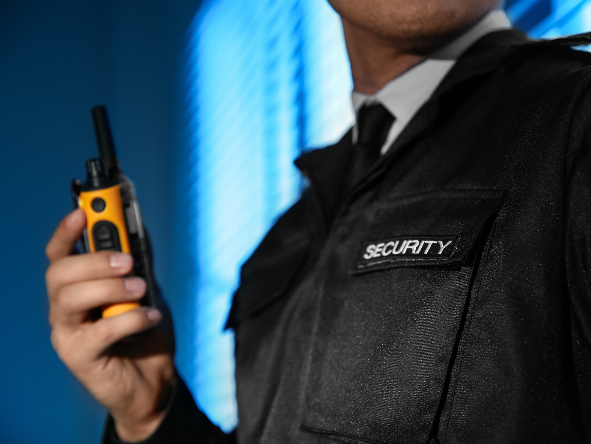 Security guard holding a walkie-talkie, wearing a black uniform with a 