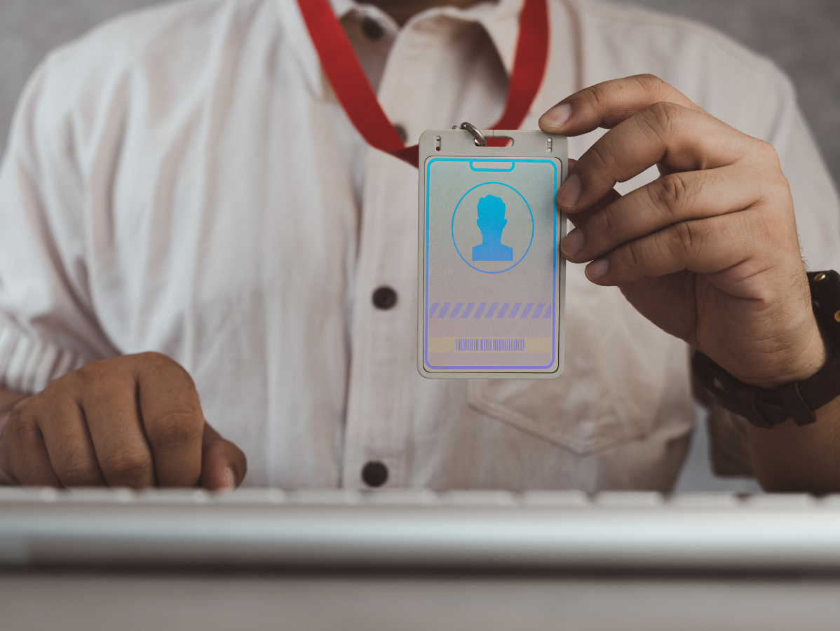 Person holding a glowing ID badge with a blue profile icon, near a keyboard.