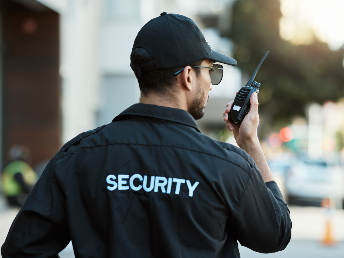 Security guard in black uniform, holding a radio, looking to the right.