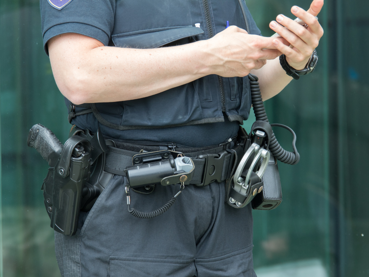 Police officer in uniform, hands adjusting gear on utility belt.